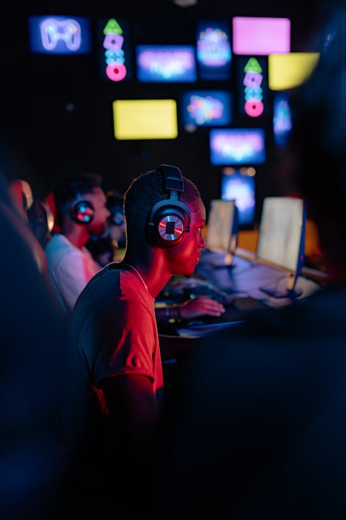 African American man gaming intensely on computer with headphones in vibrant setting.