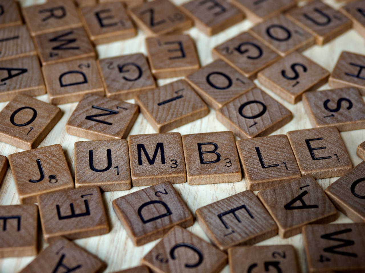 Close-up of scattered Scrabble tiles forming the word jumble on a wooden surface.